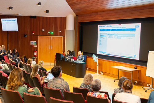 People sat in rows in Lecture Theatre looking at a screen showing demonstration of new electronic patient record